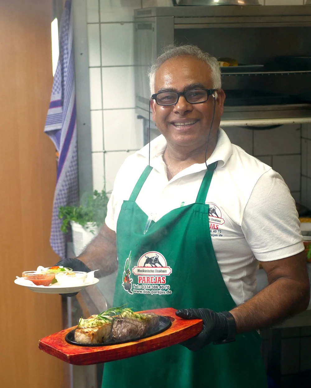 Host of Parejas holding a steak on a hot cast-iron plate in the kitchen